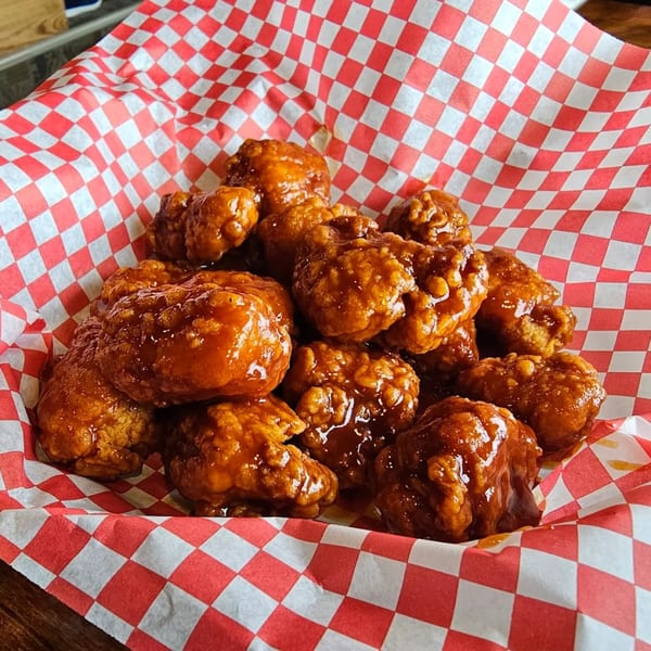 A basket of crispy, saucy boneless chicken wings in a red and white checkered paper liner.